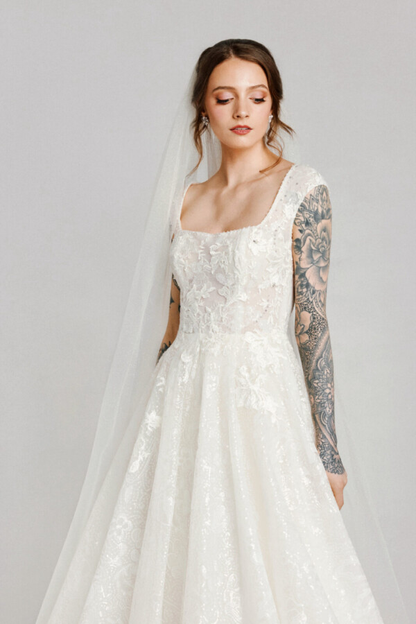 A bride with tattoos in a white fitted slim floral lace dress with a veil.