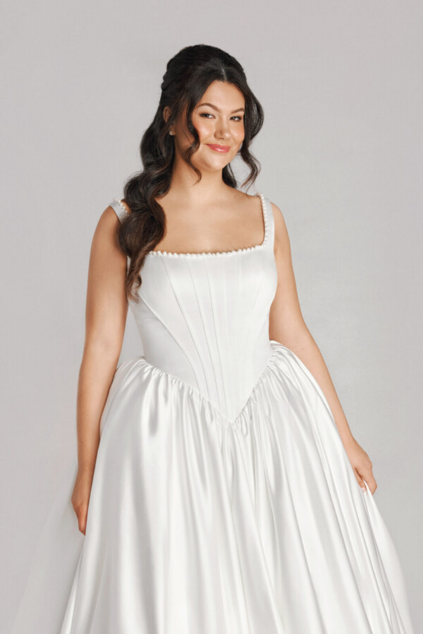 A bride in a white fitted and plated dress.