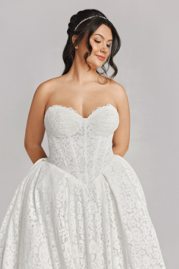 A bride in a white fitted strapless floral lace dress.