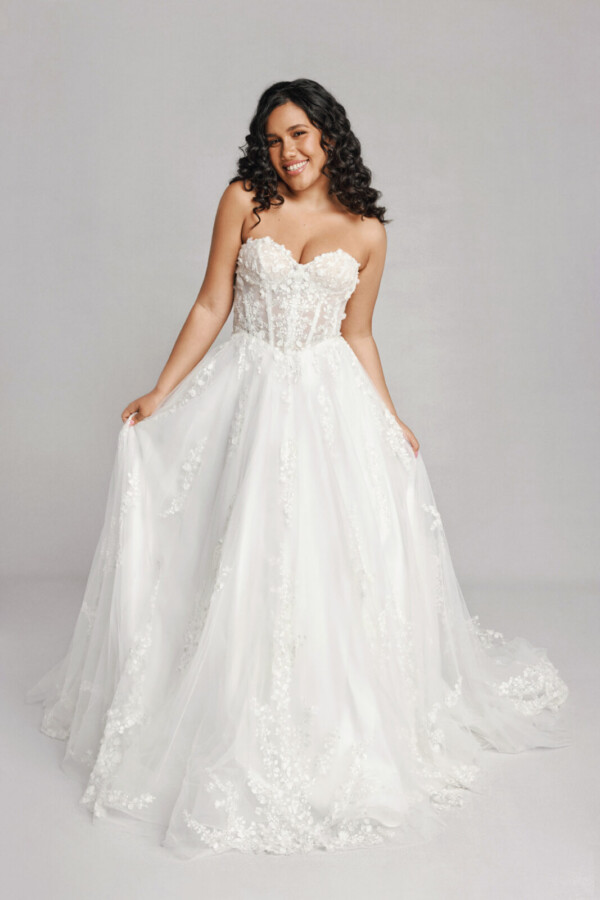 A bride in a white fitted strapless floral lace dress.