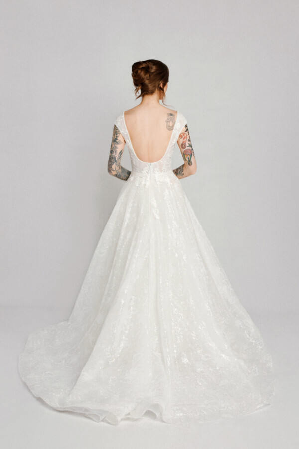 A bride with tattoos in a open back white fitted slim floral lace dress.