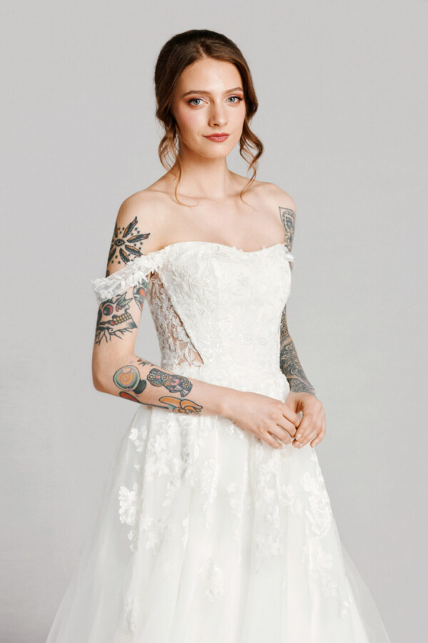 A bride with tattoos in a white fitted off the shoulder dress.