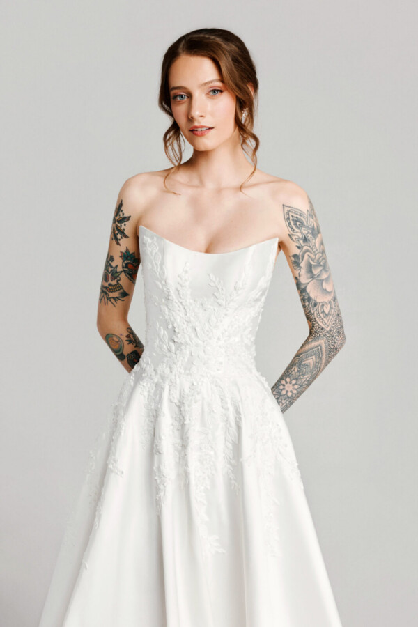 A bride with tattoos in a white fitted slim strapless dress.