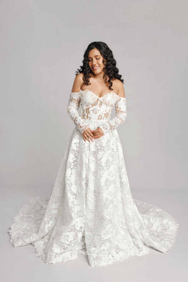 A bride in a white sheer floral long sleeve fitted off the shoulder dress.