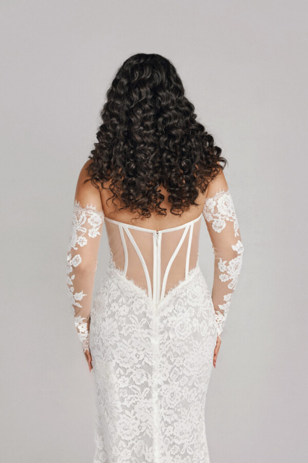 A bride in a white flowy sheer long sleeve floral open back dress.