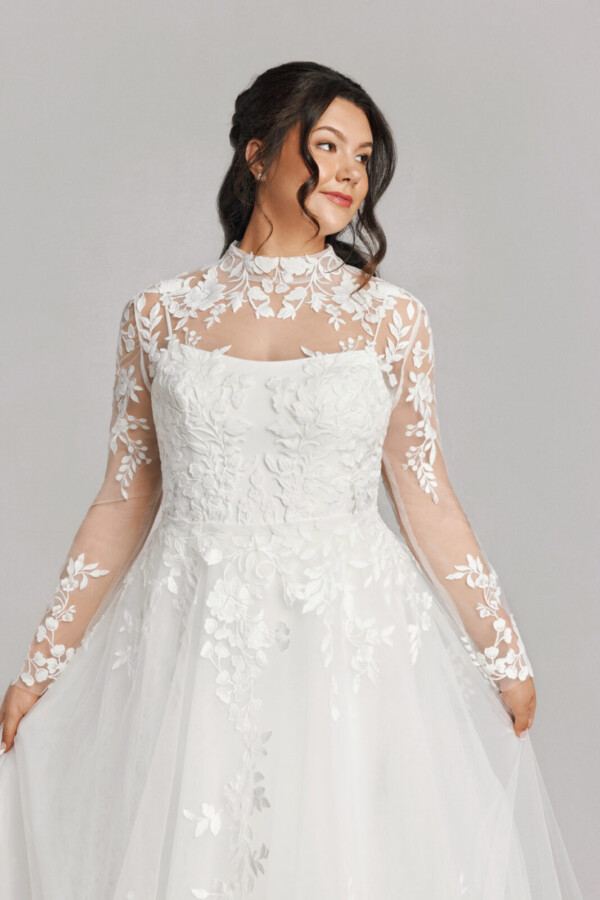 A bride in a white fitted slim strap floral lace dress with sheer floral sleeves.