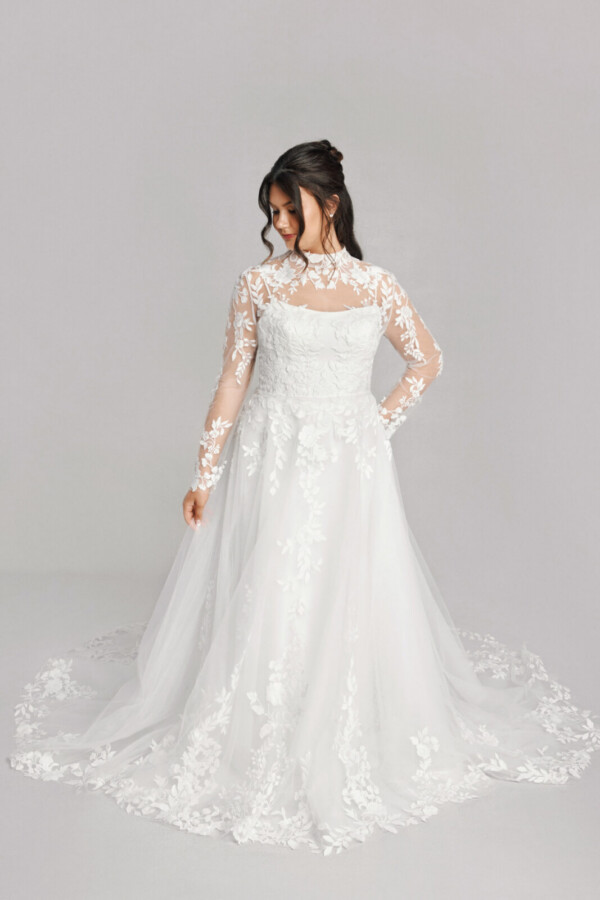 A bride in a white fitted slim strap floral lace dress with sheer floral sleeves.