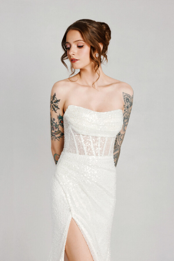 A bride with tattoos in a white fitted lace floral dress with leg slit.