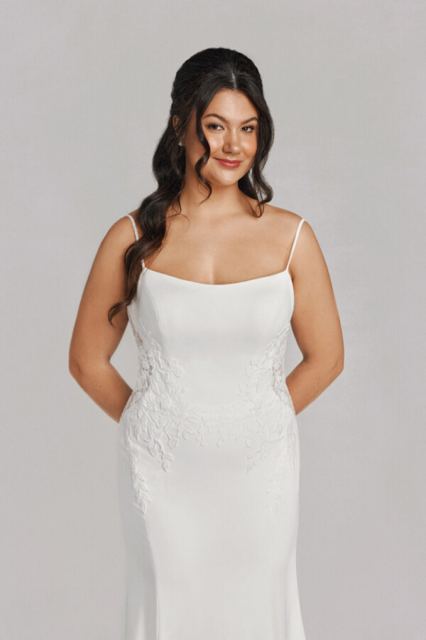 A bride in a white fitted slim strap floral lace dress.