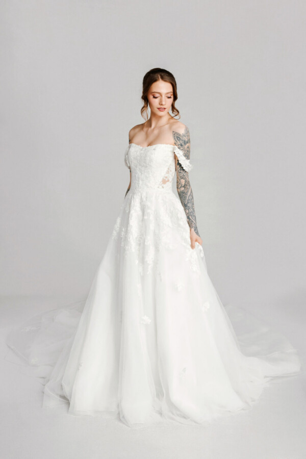 A bride with tattoos in a white fitted off the shoulder dress.