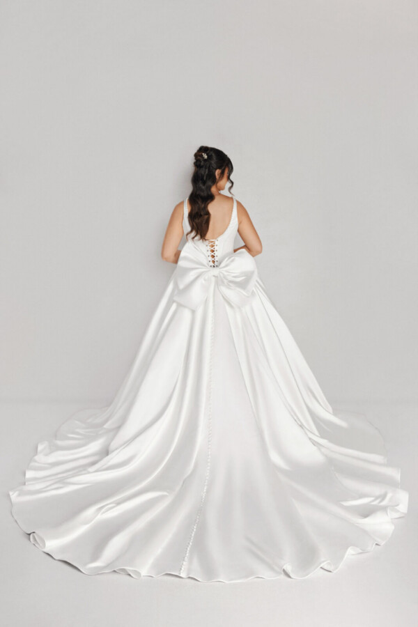 A bride in a white fitted and plated dress with a bow on the back.