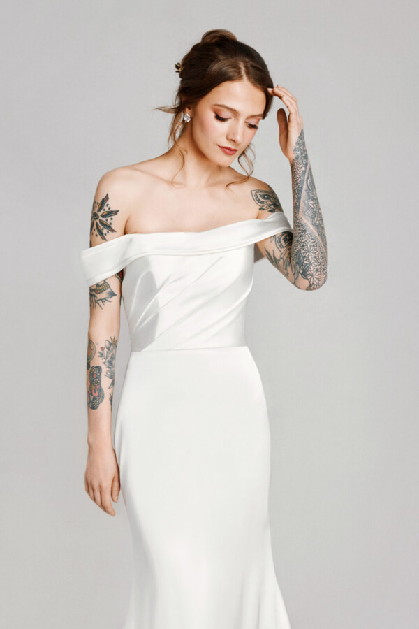 A bride with tattoos in a white fitted off the shoulder dress.
