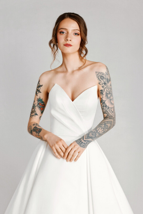 A bride with tattoos in a white fitted slim strapless dress.
