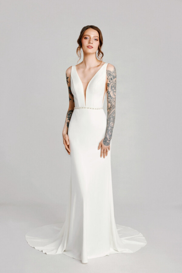 A bride with tattoos in a white fitted deep v cut slim backless dress.