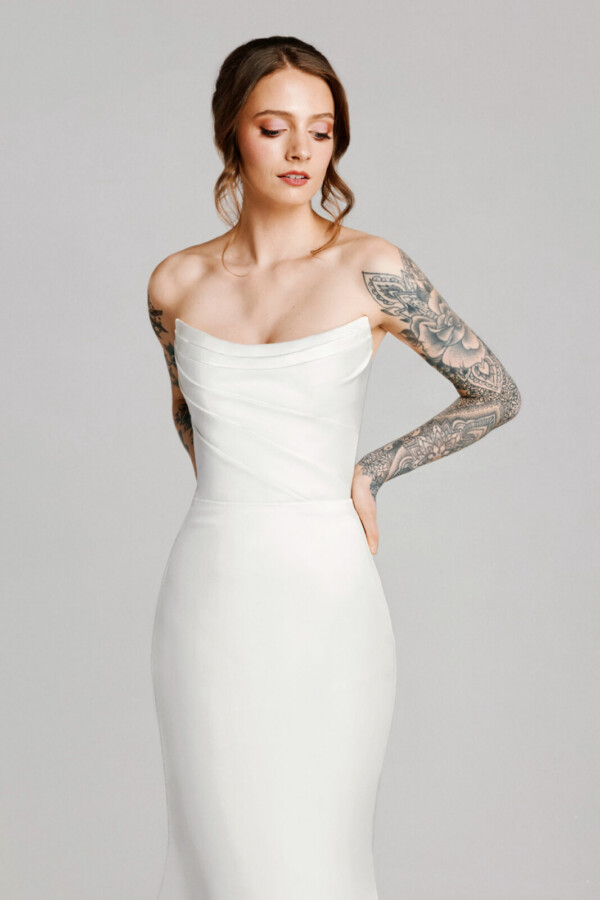 A bride with tattoos in a white fitted slim strapless wedding dress.