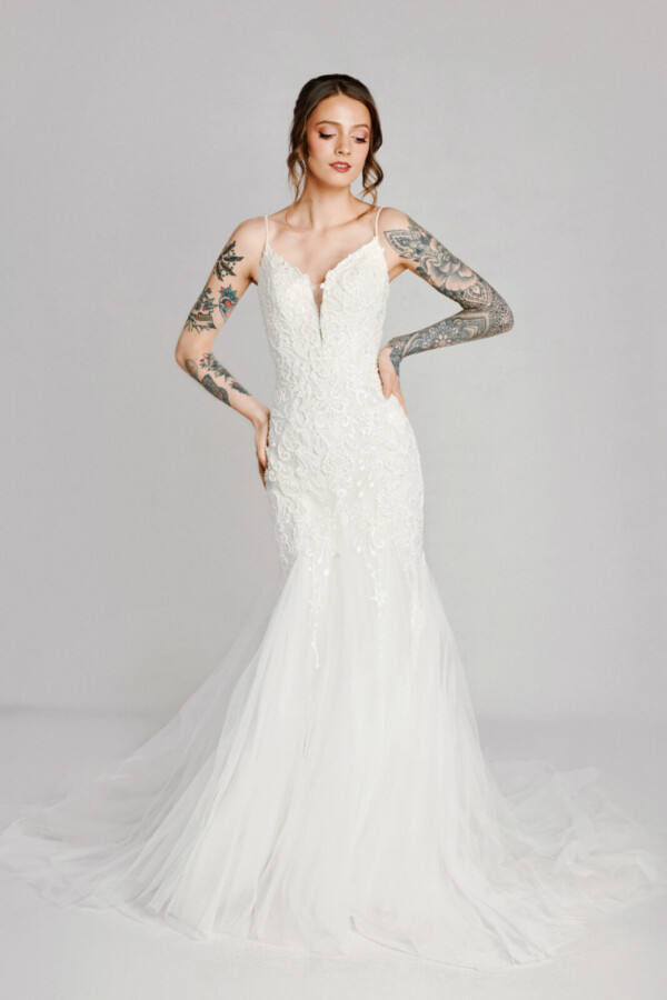 A bride with tattoos in a white fitted slim strapped deep v cut dress.