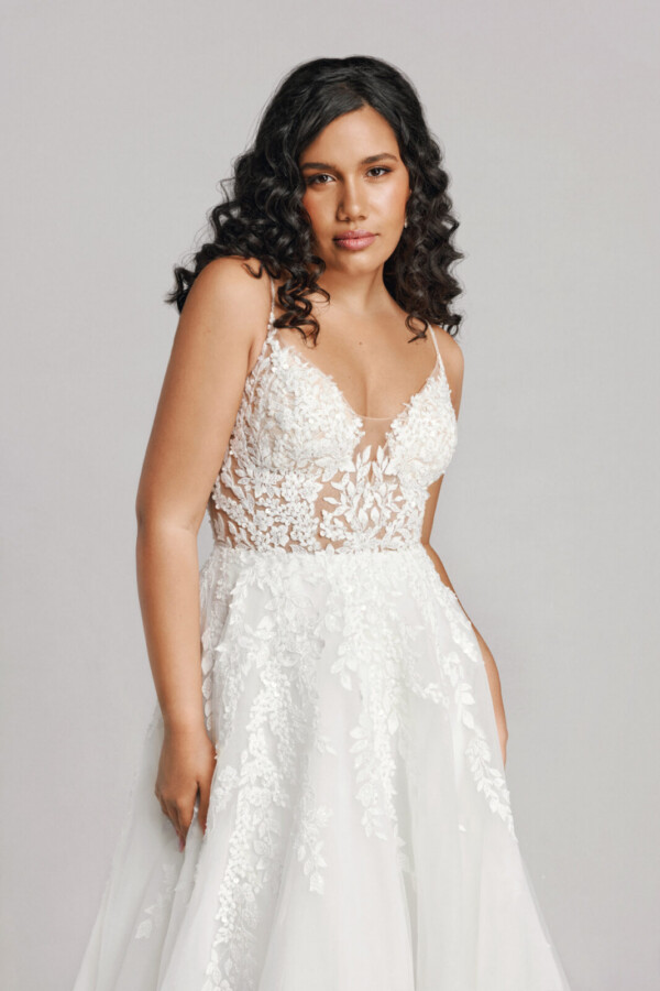 A bride in a white fitted slim strapped floral lace dress.