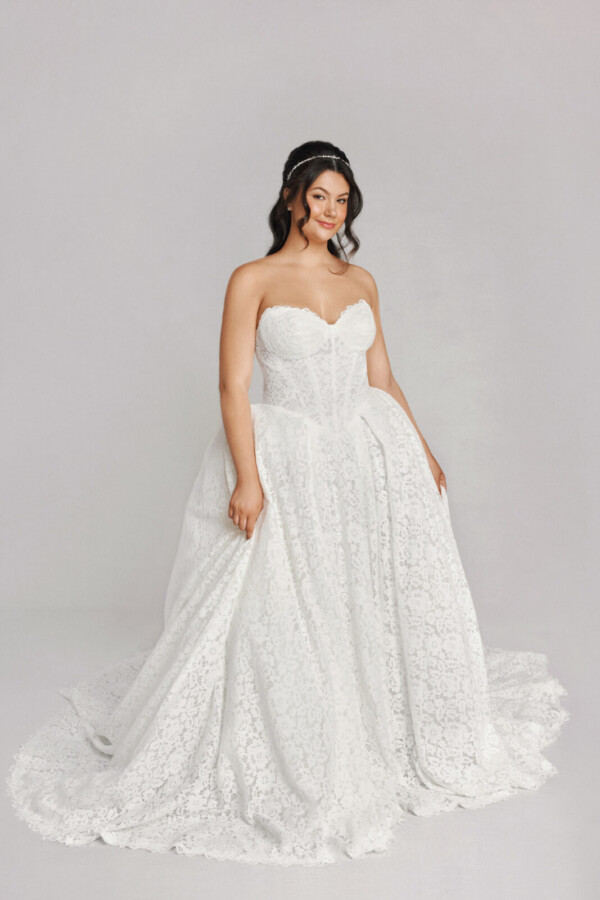 A bride in a white fitted strapless floral lace dress.