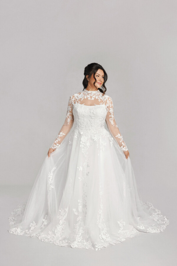 A bride in a white fitted slim strap floral lace dress with sheer floral sleeves.