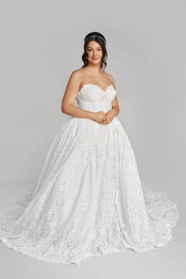 A bride in a white fitted strapless floral lace dress.