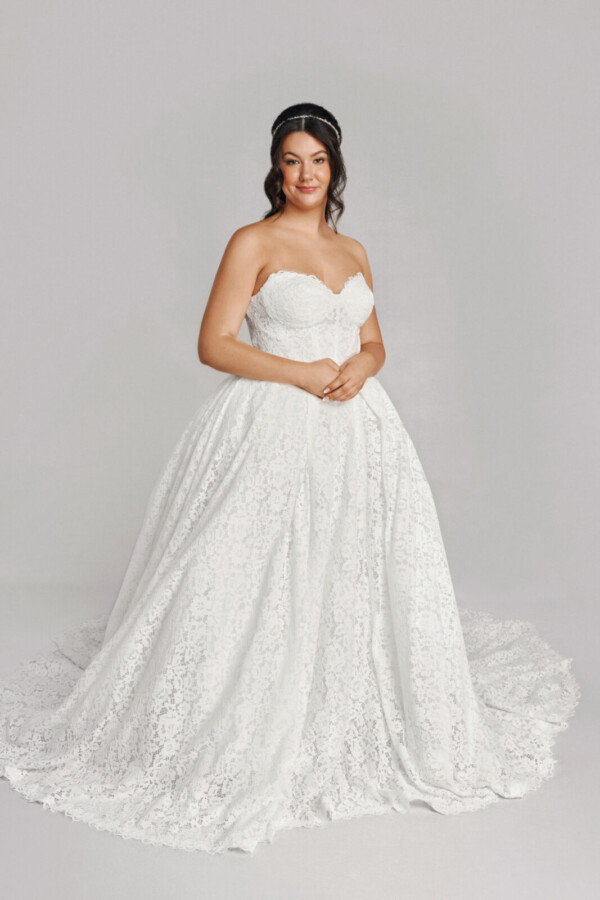 A bride in a white fitted strapless floral lace dress.