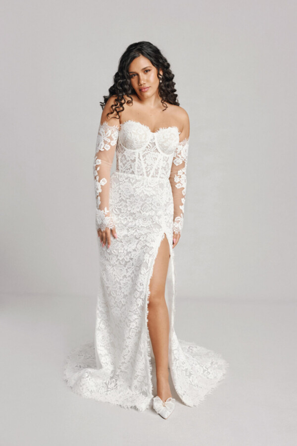 A bride in a white flowy sheer long sleeve floral open back dress with leg slit.