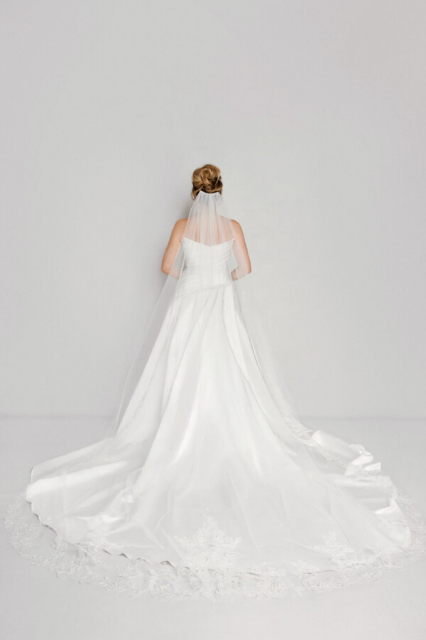 A bride in a white fitted slim strapless dress with a bridal veil.