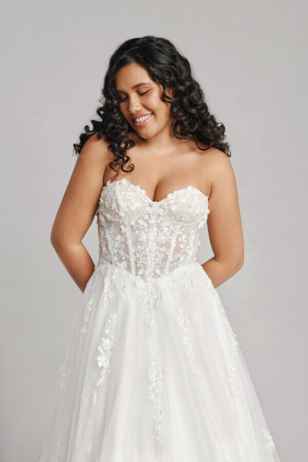 A bride in a white fitted strapless floral lace dress.