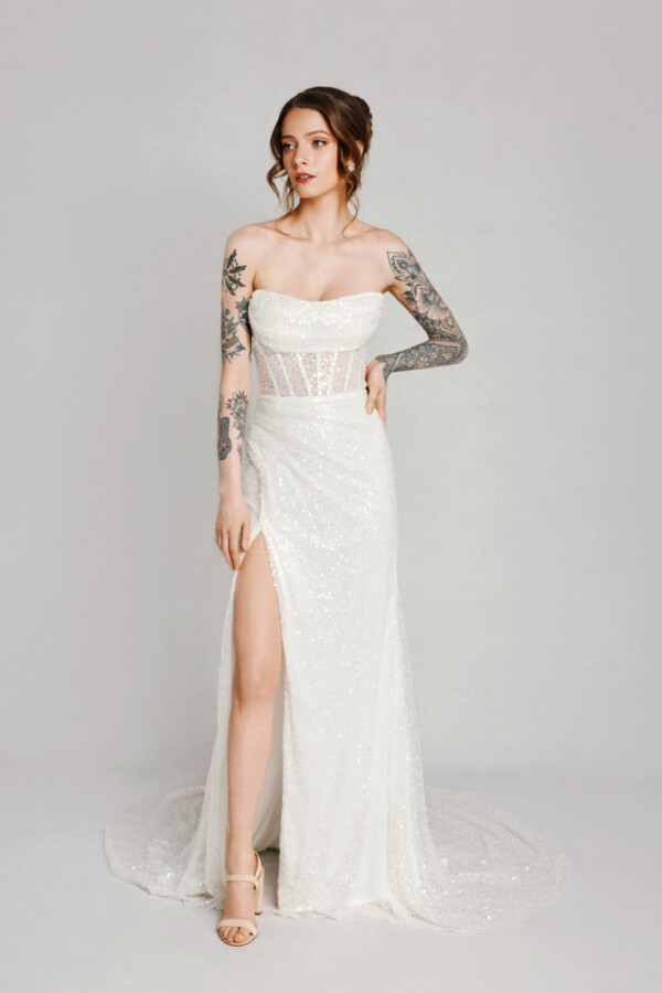 A bride with tattoos in a white fitted lace floral dress with leg slit.