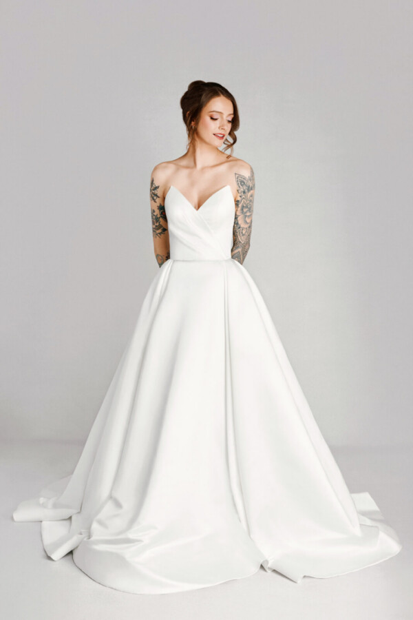 A bride with tattoos in a white fitted slim strapless dress.