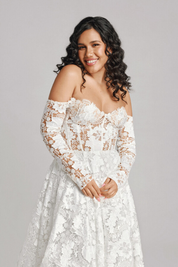 A bride in a white sheer floral long sleeve fitted off the shoulder dress.
