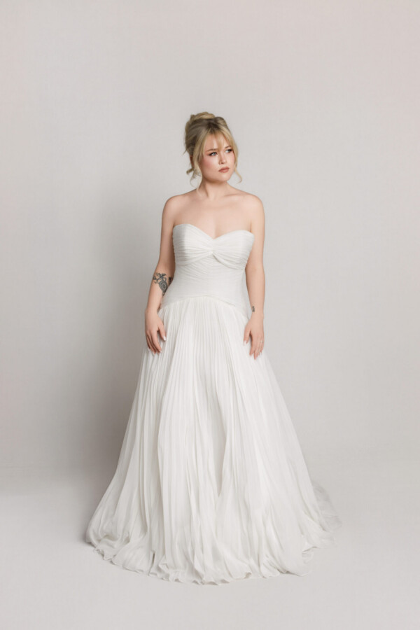 Bride in a strapless tulle wedding dress with a sweetheart neckline and flowing skirt, posing against a neutral background.