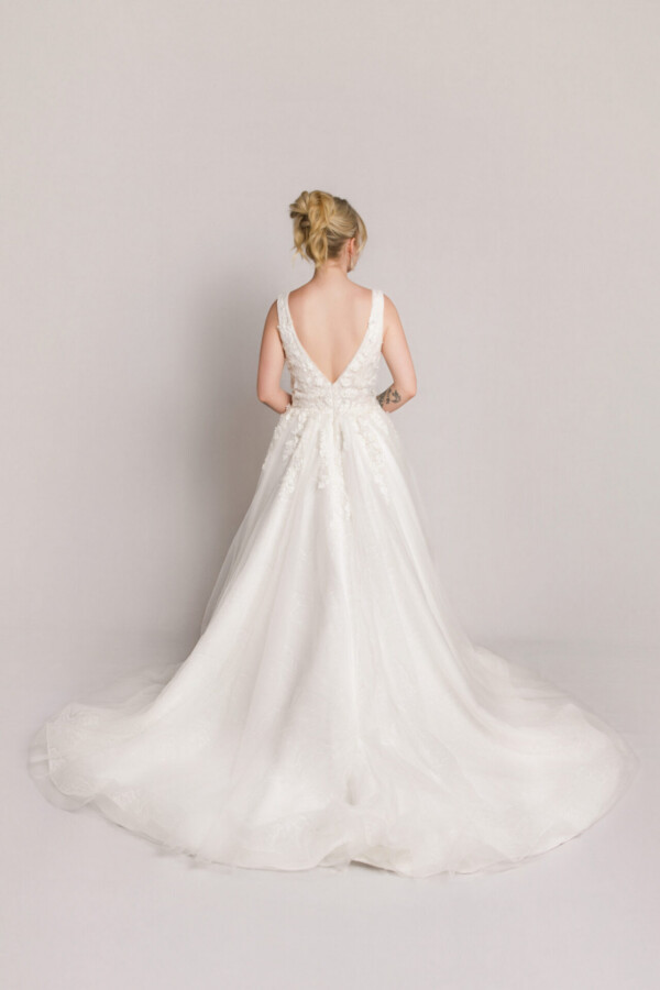 Back view of a bride in a sleeveless lace wedding gown with a deep V-back and a soft tulle skirt with a flowing train.
