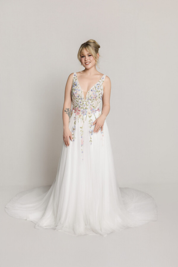 Bride wearing a sleeveless lace bodice wedding gown with a flowing skirt, standing against a neutral background.