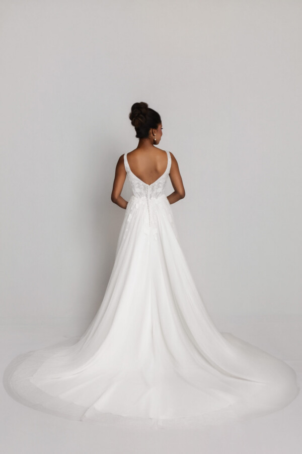 Back view of a bride in a white wedding gown with thin straps and a flowing train spread out behind her.