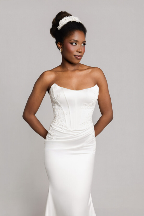 Bride wearing a strapless fitted white wedding gown with hair in an updo, posing against a neutral background.