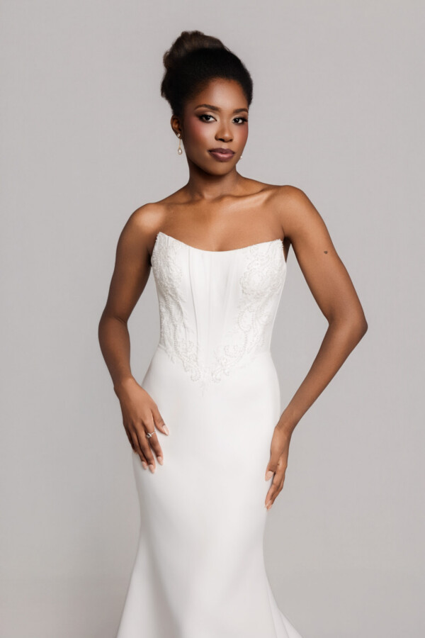 Close-up of a bride in a strapless fitted white gown with a structured bodice, posing against a neutral backdrop.