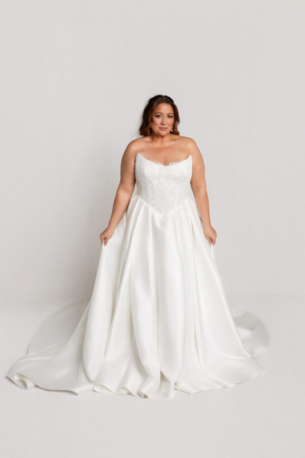 Bride wearing a strapless white wedding gown with a sweetheart neckline and full flowing skirt, standing against a neutral background.