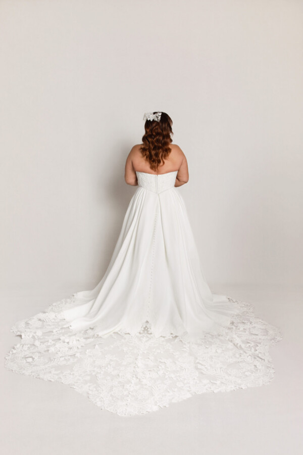 Back view of a bride in a strapless lace wedding gown with a long detailed train spread out on the floor.