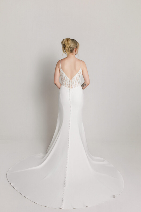 Back view of a bride in a fitted white gown with thin straps and a long, narrow train.