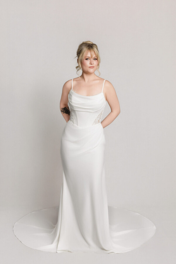 Bride in a sleek white wedding dress with thin straps and a fitted silhouette, standing with a slight train.