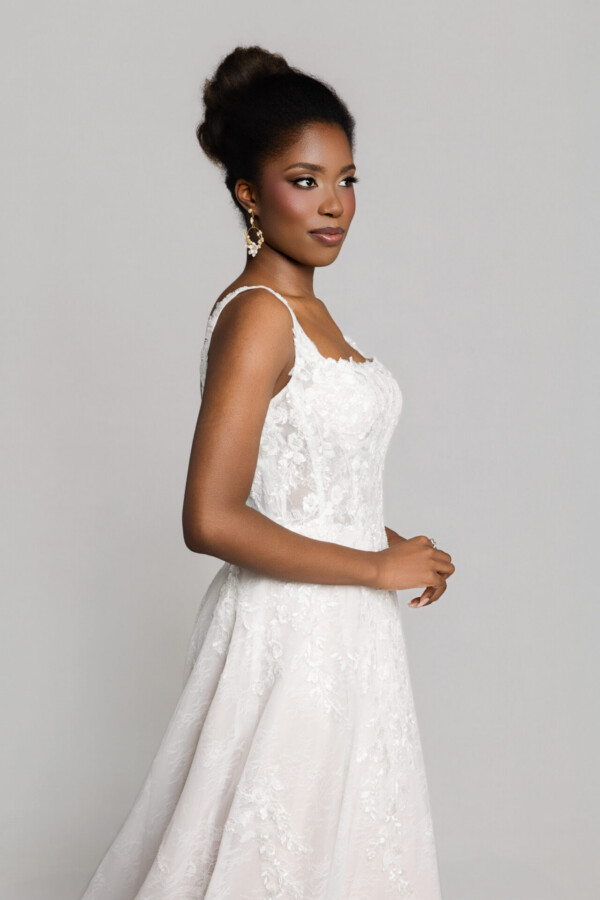 Close-up side view of a bride in a lace wedding dress with thin straps, wearing statement earrings and an updo hairstyle.