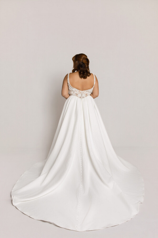 Back view of a bride in a white wedding gown with thin straps, a detailed bodice, and a long flowing train.