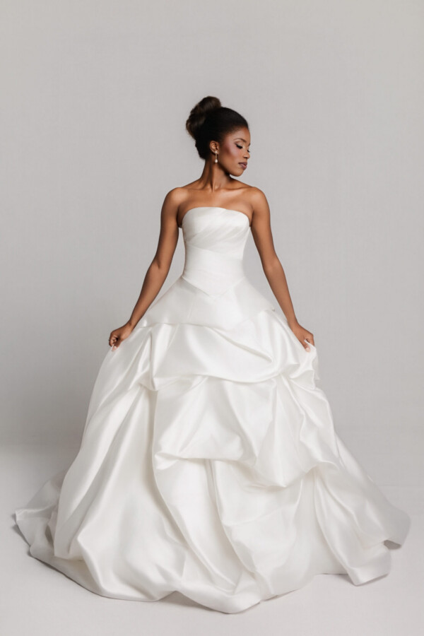 Bride in a strapless gown with a layered, voluminous skirt, holding the sides of the dress while standing.