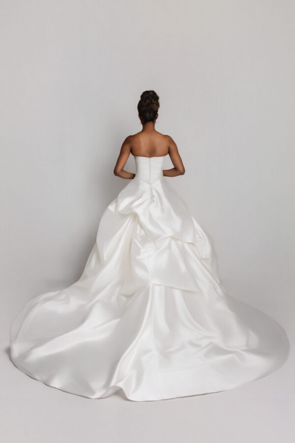 Back view of a bride in a strapless wedding gown with a full, structured skirt and long train spread out behind her.
