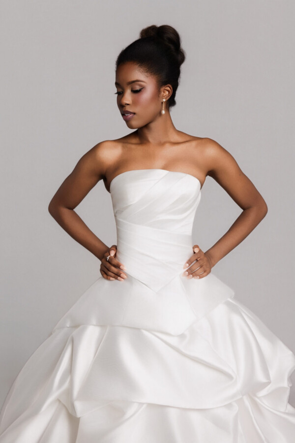 Bride wearing a strapless white wedding gown with a structured bodice and hands on hips, against a neutral background.