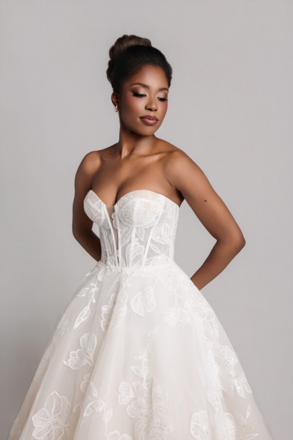 Close-up of a bride in a strapless lace wedding gown with a structured bodice, posing with hands behind her back.