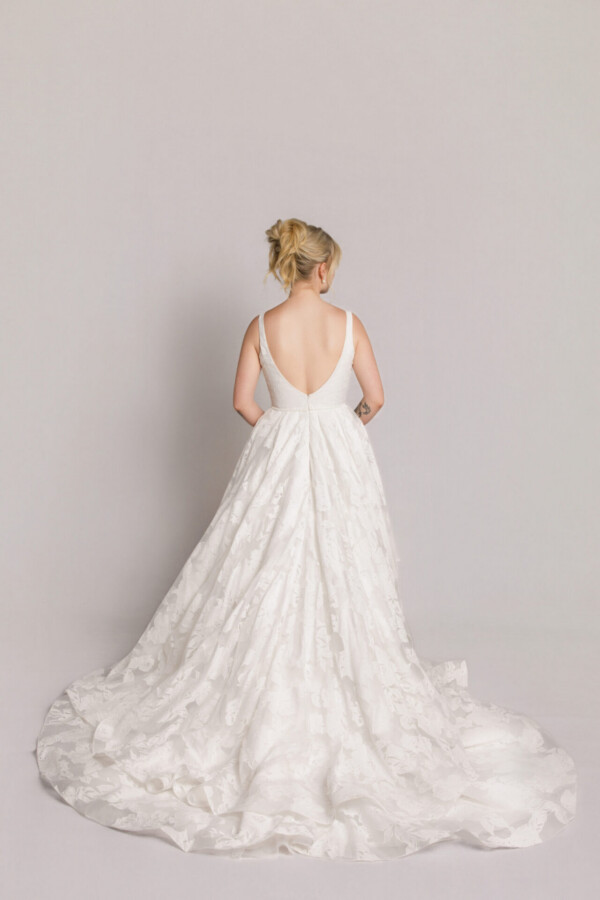 Back view of a bride in a lace wedding gown with a low back and full train spread across the floor.