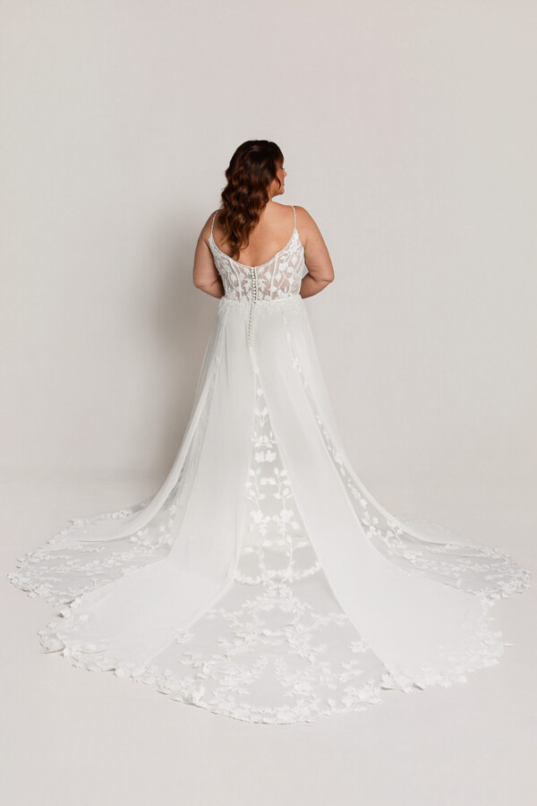 Back view of a bride in a lace wedding gown with thin straps and a long sheer train featuring floral detailing.