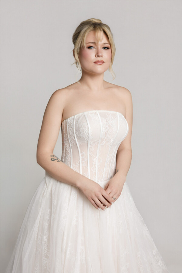 Close-up of a bride wearing a strapless lace corset-style wedding gown with a structured bodice and full tulle skirt.